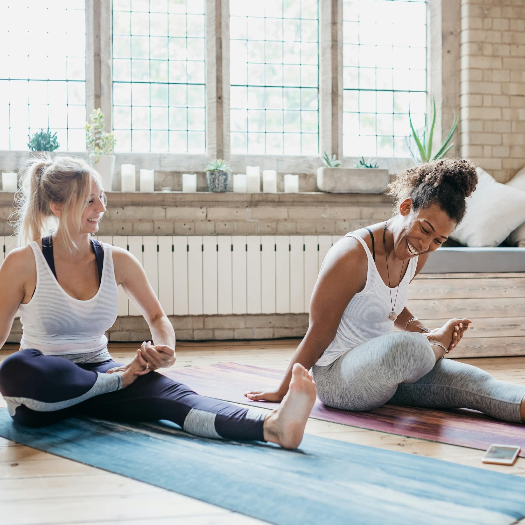 Two happy women doing online yoga with a phone in a well-lit appartment